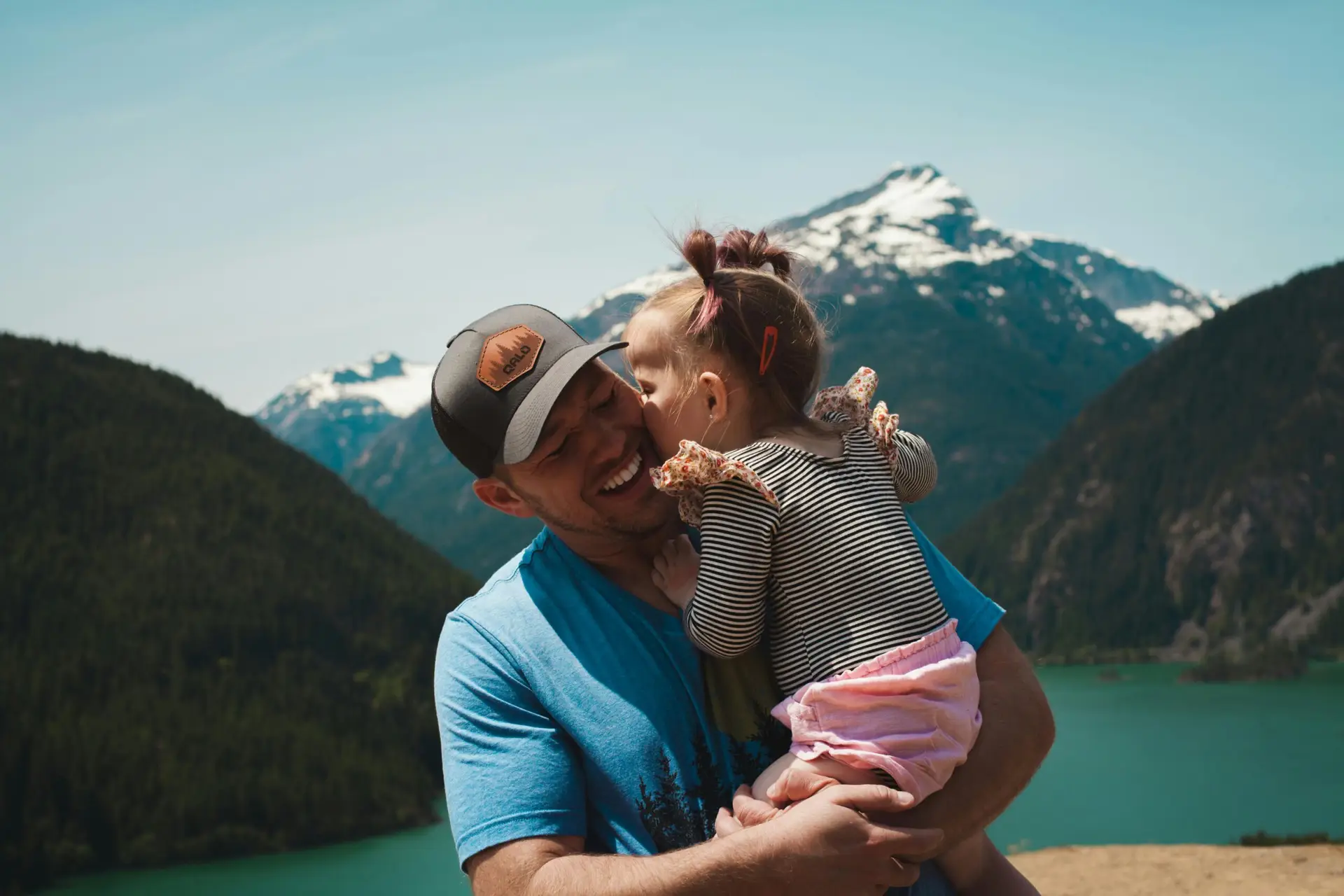 Tender moment of a father and daughter hugging in a scenic mountain setting.